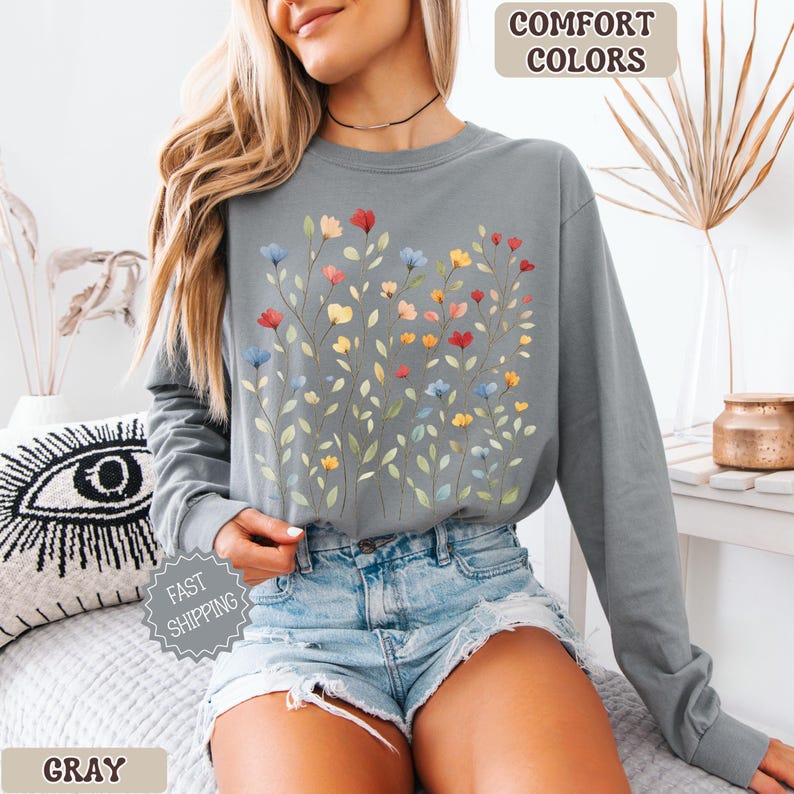 May include: Gray long-sleeve shirt with a floral design. The shirt features a watercolor-style illustration of colorful flowers in red, yellow, and blue. The words "Comfort Colors" and "Gray" are visible.