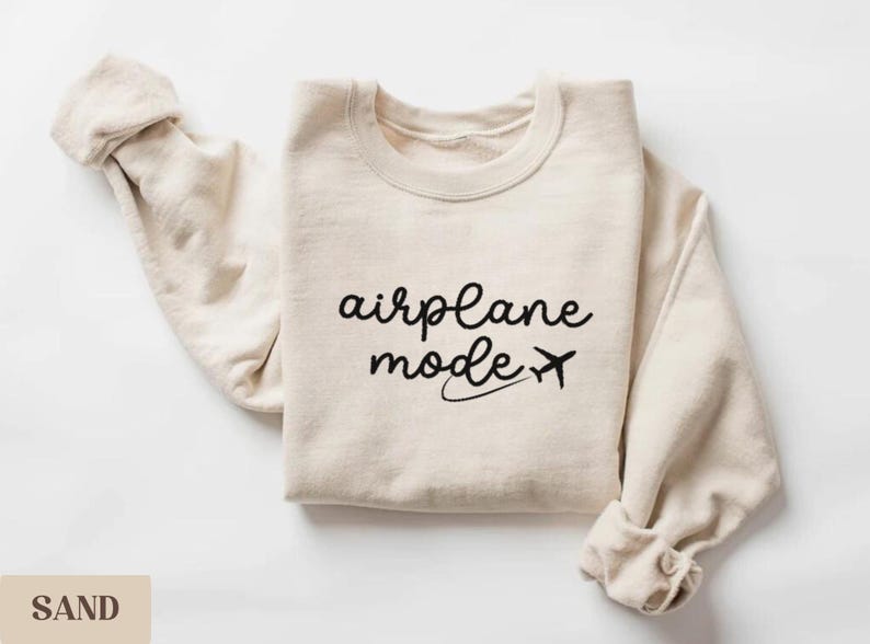 Puede incluir: Una sudadera beige con el texto "airplane mode" y un peque&ntilde;o avi&oacute;n impreso en negro.