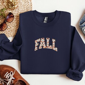 May include: Navy blue sweatshirt with a white and brown "FALL" graphic made of autumn leaves.