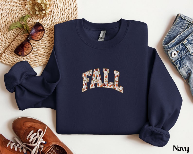 May include: Navy blue sweatshirt with a white and brown "FALL" graphic made of autumn leaves.