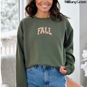 May include: A green sweatshirt with the word "FALL" printed in brown and white on the front. The letters are made up of a pattern of leaves and acorns.