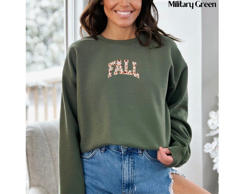 May include: A green sweatshirt with the word "FALL" printed in brown and white on the front. The letters are made up of a pattern of leaves and acorns.
