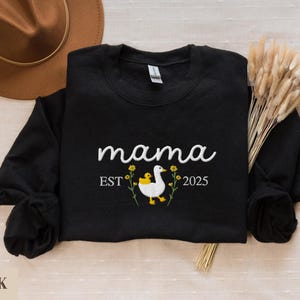 May include: Black sweatshirt with the text "mama est 2025" and an embroidered image of a white duck with a yellow duckling on its back.