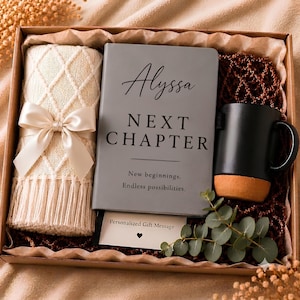 Peut inclure: Un coffret cadeau contenant une couverture en tricot crème avec un nœud en satin, un carnet gris avec le texte Alyssa NEXT CHAPTER New beginnings. Endless possibilities., un mug noir à base beige et une carte Personalized Gift Message.