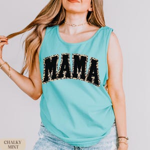 May include: A turquoise tank top with a black "MAMA" graphic. The graphic is outlined in a leopard print pattern.