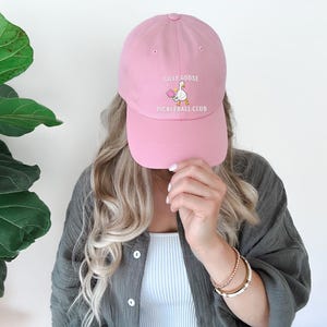 May include: A pink baseball cap with the text "Silly Goose Pickleball Club" and a cartoon goose holding a pickleball paddle.