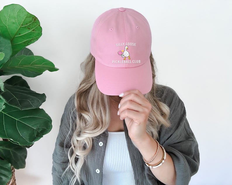 May include: A pink baseball cap with the text "Silly Goose Pickleball Club" and a cartoon goose holding a pickleball paddle.