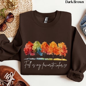 May include: Dark brown sweatshirt with a watercolor design of five colorful trees and the text "Fall is my favorite color" with a heart.