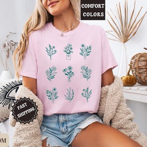 May include: A pink t-shirt with a graphic of nine different floral designs in green. The text "COMFORT COLORS" is on a white tag attached to the shirt. The text "FAST SHIPPING" is on a black tag.