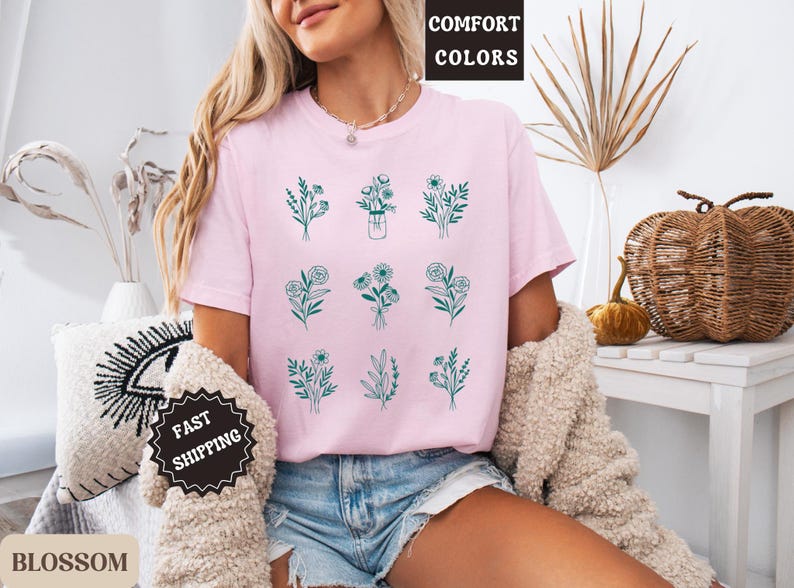 May include: A pink t-shirt with a graphic of nine different floral designs in green. The text "COMFORT COLORS" is on a white tag attached to the shirt. The text "FAST SHIPPING" is on a black tag.