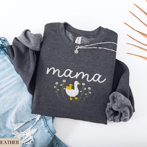 May include: Dark heather grey sweatshirt with white embroidery that says "mama" and a white duck with a yellow chick on its back. The duck is surrounded by small white flowers.