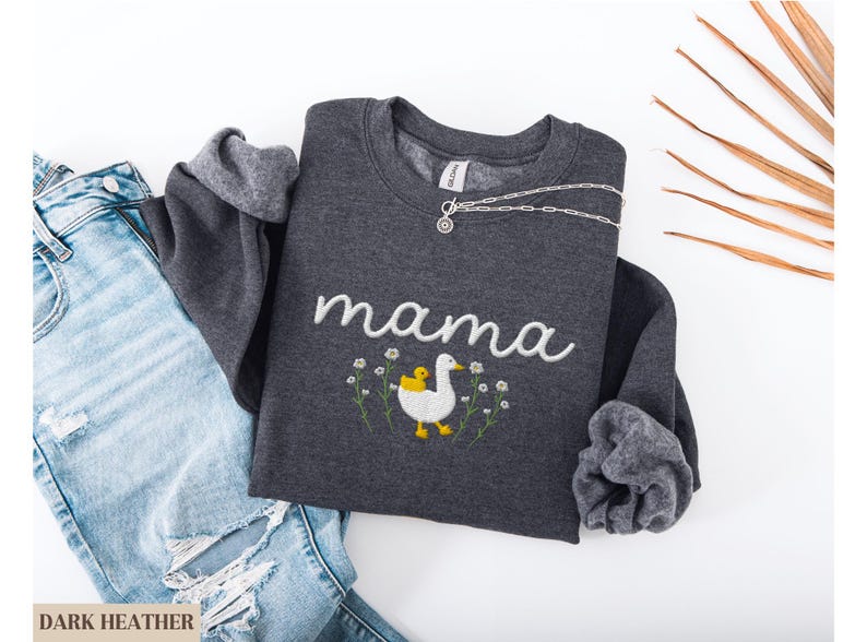 May include: Dark heather grey sweatshirt with white embroidery that says "mama" and a white duck with a yellow chick on its back. The duck is surrounded by small white flowers.