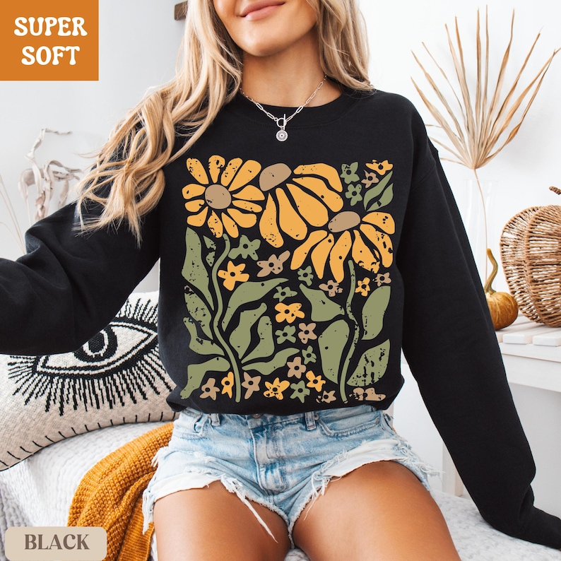 May include: A black long-sleeve sweatshirt featuring a large graphic print of yellow sunflowers and green leaves. The design has a distressed, textured appearance. The sweatshirt has a crew neckline and long sleeves, providing a casual look.