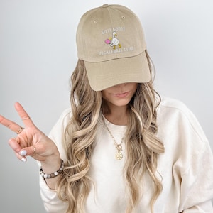 May include: A beige baseball cap with an embroidered white goose holding a pink ball and the text "Silly Goose Pickleball Club".
