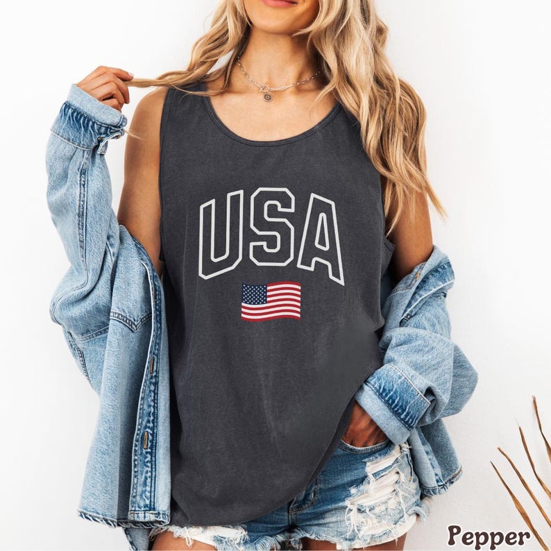 Peut inclure: D&eacute;bardeur gris fonc&eacute; avec le mot "USA" en lettres blanches et un petit drapeau am&eacute;ricain. Le d&eacute;bardeur est sans manches et a une encolure d&eacute;gag&eacute;e.