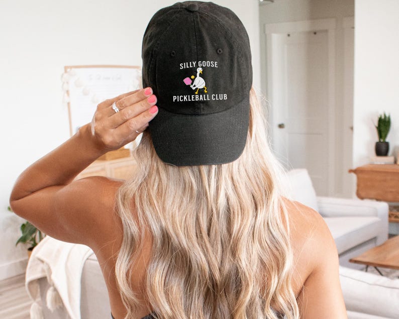 May include: Black baseball cap with white embroidery that reads "Silly Goose Pickleball Club". The embroidery also features a cartoon goose holding a pickleball paddle.