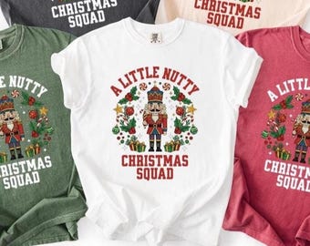 May include: Several Christmas-themed t-shirts in white, green, red, and grey. Each shirt displays a nutcracker graphic and the text "Christmas Squad" or "A Little Nutty Christmas Squad". Festive apparel for the holiday season.