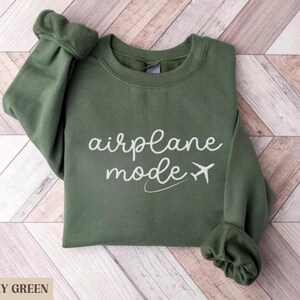 Puede incluir: Una sudadera verde con el texto "modo avi&oacute;n" en letras blancas y un peque&ntilde;o gr&aacute;fico de avi&oacute;n.