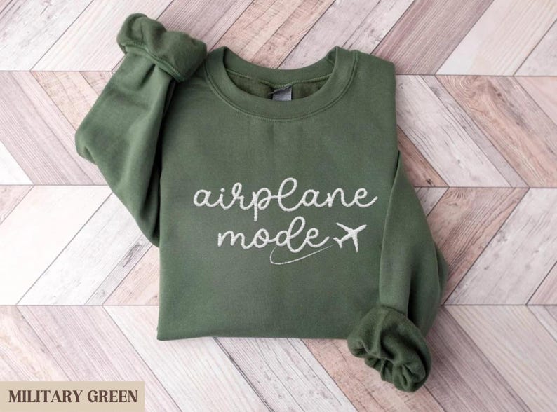 Puede incluir: Una sudadera verde con el texto "modo avi&oacute;n" en letras blancas y un peque&ntilde;o gr&aacute;fico de avi&oacute;n.