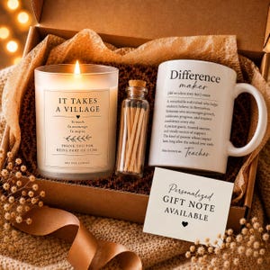May include: A gift box containing a lit soy wax candle with the text It Takes A Village, a small glass bottle filled with wooden matches, a white ceramic mug with the text Difference Maker, and a card stating Personalized Gift Note Available.