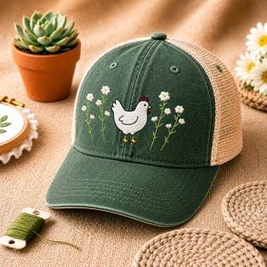 May include: A green baseball cap with a white chicken and floral embroidery. The cap has a mesh back and a curved brim. The chicken has a red comb and yellow feet. The flowers are white with green stems.