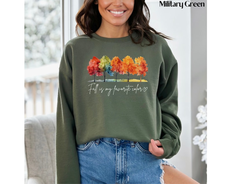 May include: A green sweatshirt with a watercolor design of colorful trees and the text "Fall is my favorite color" with a heart.