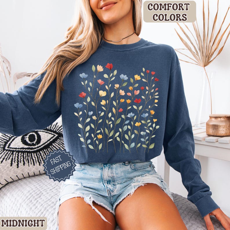 May include: A navy blue sweatshirt with a floral design featuring red, yellow, and blue flowers. The words "COMFORT COLORS" are printed at the top right. The word "MIDNIGHT" is printed at the bottom left. The words "FAST SHIPPING" are printed on a blue badge.