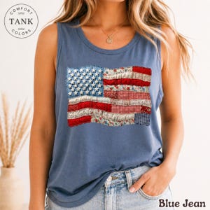 May include: Blue tank top with a patchwork American flag design. The flag features white stars on a blue background and red and white striped sections with floral and gingham patterns. The text "Blue Jean" is at the bottom.
