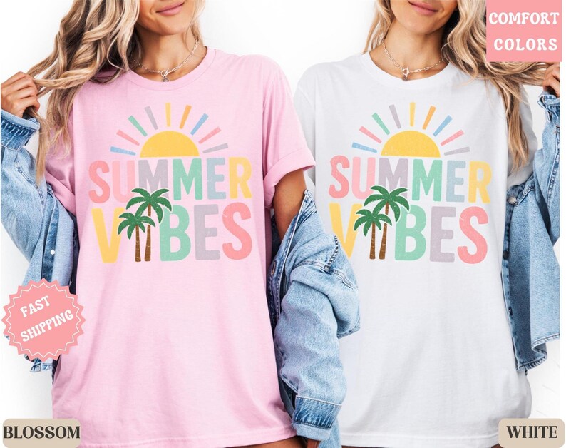 K&ouml;nnte beinhalten: Rosa und wei&szlig;e T-Shirts mit dem Text "SUMMER VIBES" in Pastellfarben, mit einer Sonne und Palmen-Grafik. Die Shirts sind Teil einer sommerlichen Bekleidungskollektion.