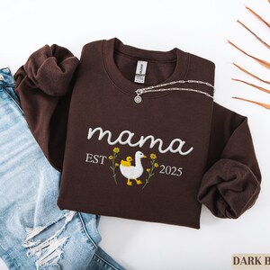 May include: Dark brown sweatshirt with the text "mama est 2025" and an embroidered image of a duck with a duckling.
