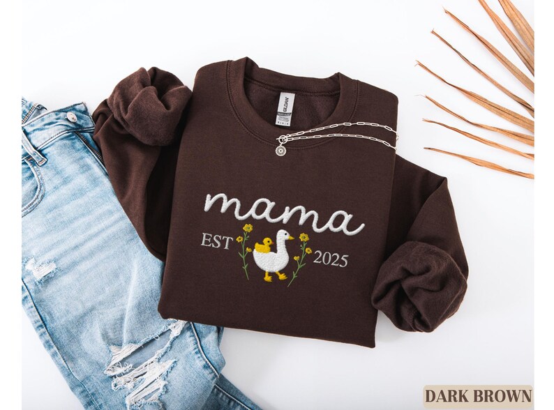 May include: Dark brown sweatshirt with the text "mama est 2025" and an embroidered image of a duck with a duckling.