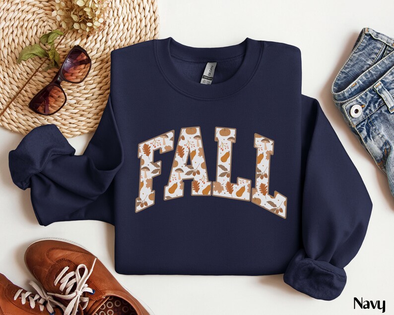 K&ouml;nnte beinhalten: Navyblauer Sweatshirt mit einem wei&szlig;en "FALL"-Motiv. Das Motiv besteht aus einem Muster aus Herbstbl&auml;ttern und Eicheln.