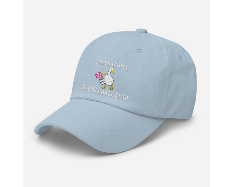 May include: A light blue baseball cap with the text "Silly Goose Pickleball Club" embroidered on the front. A cartoon goose holding a pink pickleball paddle is also embroidered on the cap.