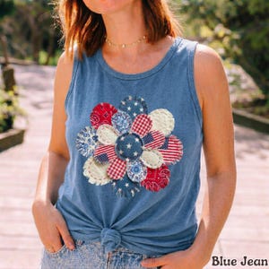 May include: Blue tank top with a floral design made of red, white, and blue fabric patches. The flower design incorporates stars and stripes, and the text "Blue Jean" is visible at the bottom right.
