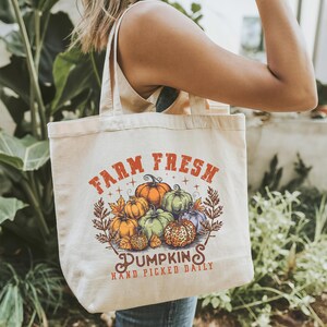 May include: A white canvas tote bag with the text "Farm Fresh" and a graphic of pumpkins. The text "Pumpkins" is below the graphic and the text "Hand Picked Daily" is below that.