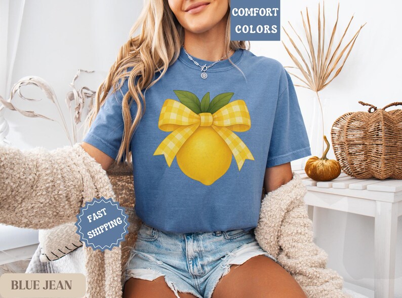 Puede incluir: Una camiseta azul vaquero con un lim&oacute;n amarillo y un lazo de cuadros amarillos y blancos. El texto "COMFORT COLORS" est&aacute; en la esquina superior derecha de la imagen.
