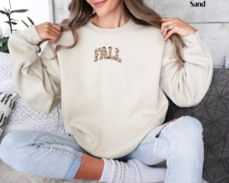 May include: A beige sweatshirt with a brown and white patterned "FALL" graphic on the front.