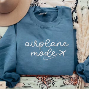 Puede incluir: Una sudadera azul con el texto "airplane mode" bordado en blanco con un peque&ntilde;o icono de avi&oacute;n.