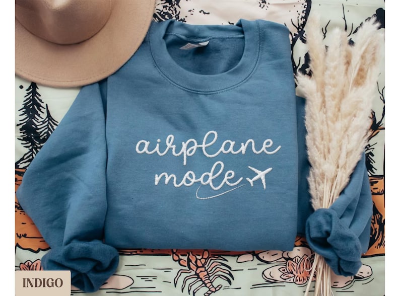Puede incluir: Una sudadera azul con el texto "airplane mode" bordado en blanco con un peque&ntilde;o icono de avi&oacute;n.
