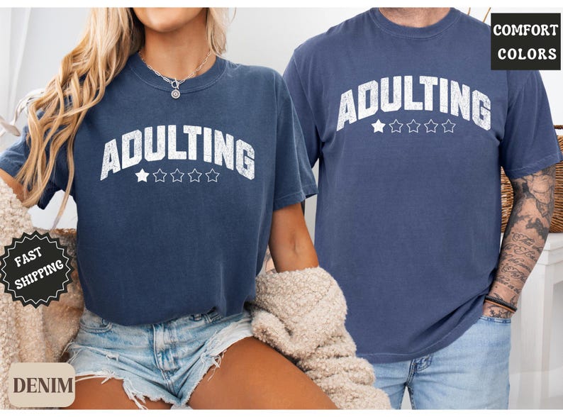 May include: Two navy blue t-shirts with the word "ADULTING" in white, arched text above five stars. The shirts are a comfortable fit, and the image includes the words "COMFORT COLORS" and "DENIM".