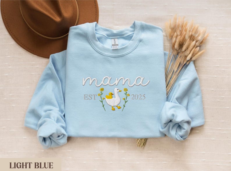 May include: Light blue sweatshirt with the text "mama est 2025" and an embroidered image of a duck with a baby duck.