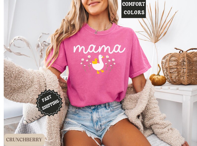 May include: Pink t-shirt with the word "mama" and a graphic of a goose with a baby goose. The shirt is made of a soft, comfortable fabric.