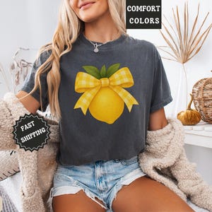 Puede incluir: Una camiseta gris oscuro con un lim&oacute;n amarillo y un lazo de cuadros. El texto "COMFORT COLORS" es visible en el fondo.