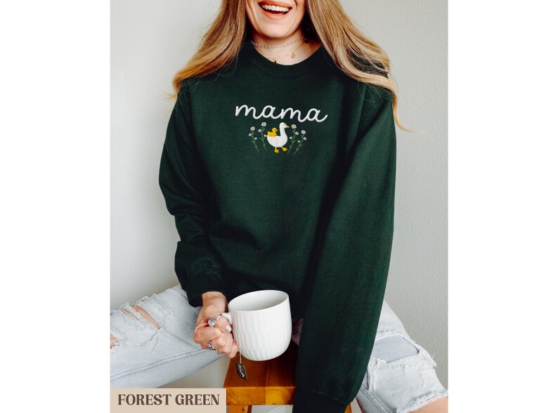 May include: A forest green sweatshirt with the word "mama" and a white duck with a yellow chick on its back embroidered on the front.