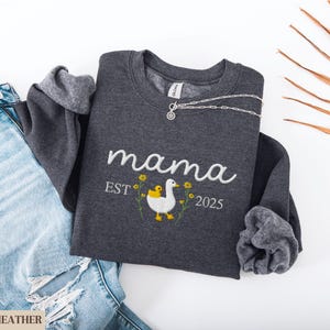 May include: Dark heather grey sweatshirt with the text "mama est. 2025" and an embroidered image of a duck and duckling.