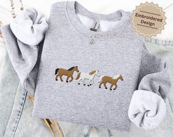 May include: A light gray sweatshirt with an embroidered design of three horses in brown and white. The sweatshirt has the text "SPORT GRAY" at the bottom. The design is labeled "Embroidered Design".