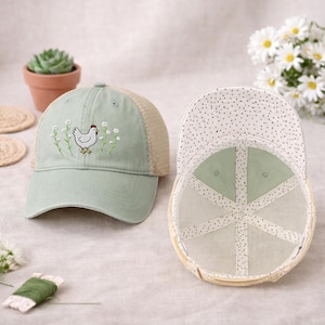 May include: A light green baseball cap with a mesh back and a white dotted pattern on the underside of the brim. The front of the cap features an embroidered chicken design with floral accents. The cap is a stylish accessory.