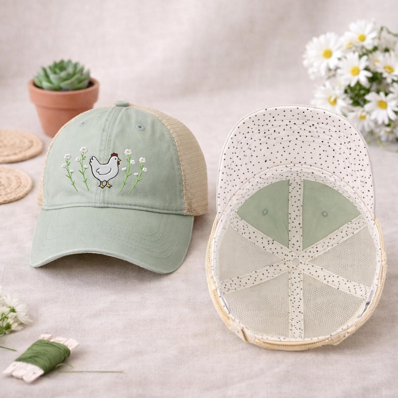 May include: A light green baseball cap with a mesh back and a white dotted pattern on the underside of the brim. The front of the cap features an embroidered chicken design with floral accents. The cap is a stylish accessory.