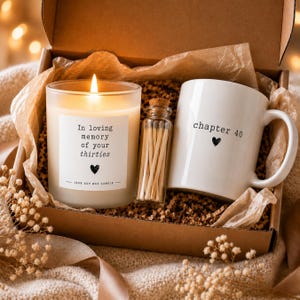May include: A gift box containing a lit soy wax candle with a label reading In loving memory of your thirties, a small glass bottle filled with wooden matches, and a white ceramic mug with the text chapter 40 and a small heart icon.