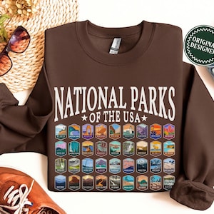 May include: Brown sweatshirt with the text "National Parks *of the USA*" in white. The sweatshirt features a grid of colorful patches representing different national parks.